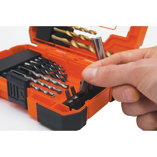 A close-up image of a hand picking a drill bit from an orange BLACK+DECKER drill bit set box containing various drill bits and accessories.