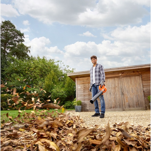 BLACKDECKER BCBL200L leaf blower in use outdoors, person clearing dry leaves from gravel path.