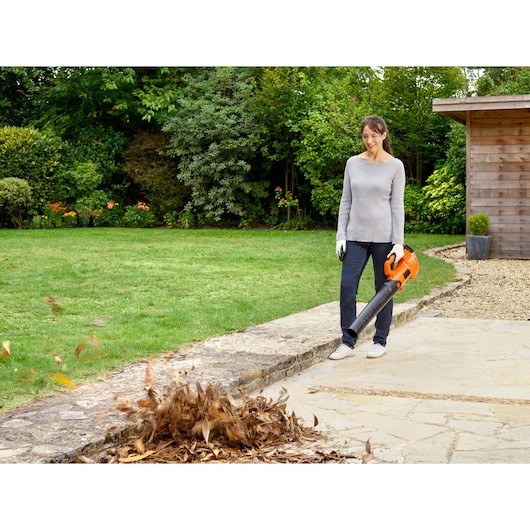 BLACKDECKER BCBL200L cordless leaf blower in use outdoors, orange design, blowing leaves on stone walkway.
