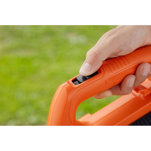 Close-up of BLACKDECKER BCBL200L orange blower handle with finger on black trigger outdoors.