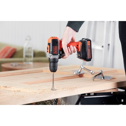 BLACK+DECKER BCD002C1 cordless drill being used to drill into a wooden board indoors, close-up view.