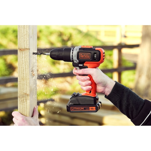 BLACK+DECKER BCD003C2K cordless drill in use, drilling into wooden post outdoors.
