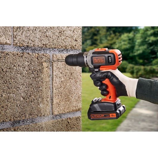 BLACKDECKER BCD003C2K cordless drill in use drilling into a brick wall outdoors.