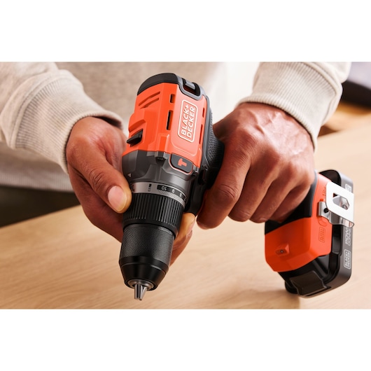 Person holding a BLACK+DECKER cordless drill on a wooden surface, showing drill details and battery.