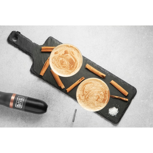 Photo of BLACK+DECKER BCKM1011KGF milk frother next to two cappuccinos with cinnamon sticks on slate board, top view.
