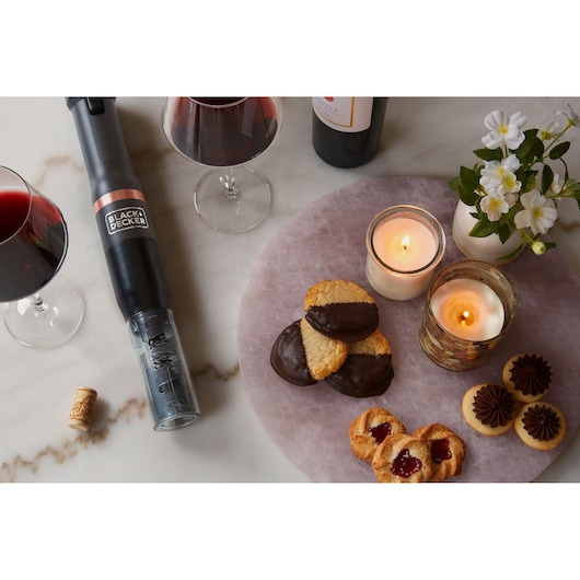 BLACK+DECKER BCKM1011KGF electric wine opener on table with wine glasses, cookies, candles, and flowers.