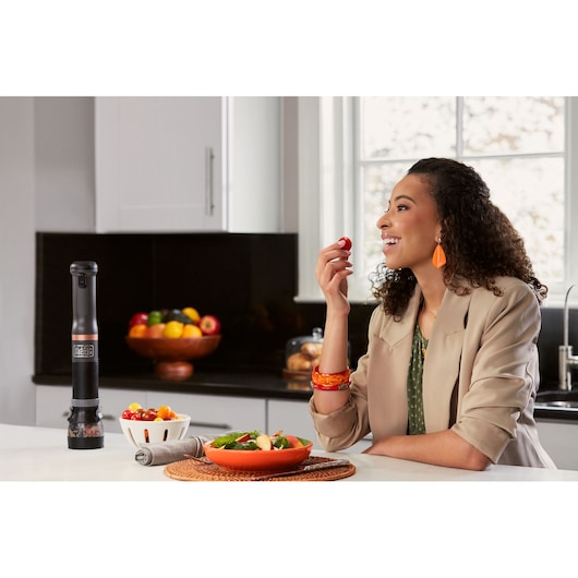 BLACKDECKER BCKM1011KGF electric pepper grinder on kitchen counter near salad bowl and woman eating tomato.