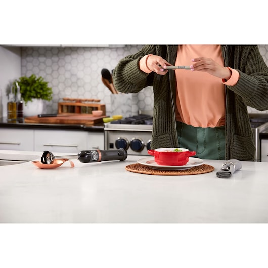 Photo of BLACKDECKER BCKM1011KGF hand blender on kitchen counter near red dish, person taking food photo.