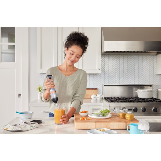 Photo of BLACKDECKER BCKM1012KG hand blender in use blending orange liquid at a kitchen counter near vegetables.