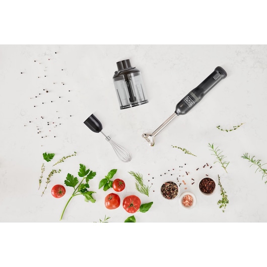 Photo of BLACKDECKER BCKM1013KB hand blender with whisk and chopper attachments, herbs, tomatoes, and spices on white surface.