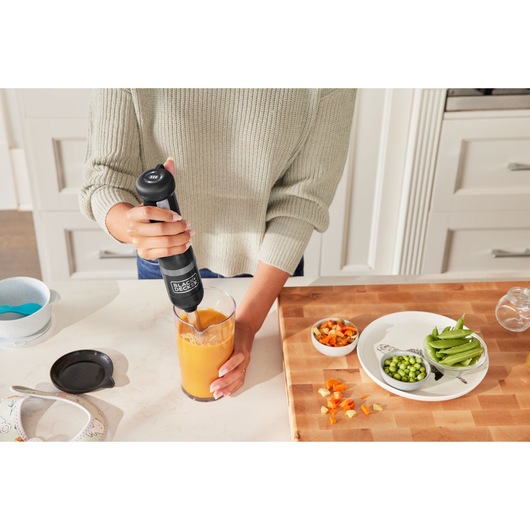 BLACKDECKER BCKM1016KSB hand blender blending orange liquid in a kitchen setting with cutting board and vegetables.