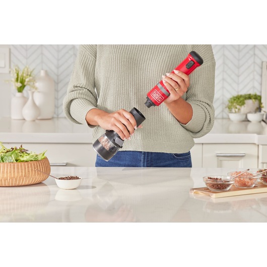 Photo of a person using a BLACKDECKER BCKM1016KSR electric grinder in a kitchen, preparing food on a counter.