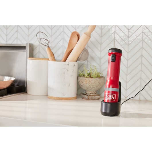 Photo of BLACKDECKER BCKM1016KSR handheld mixer in red on a kitchen counter, charging in its base.