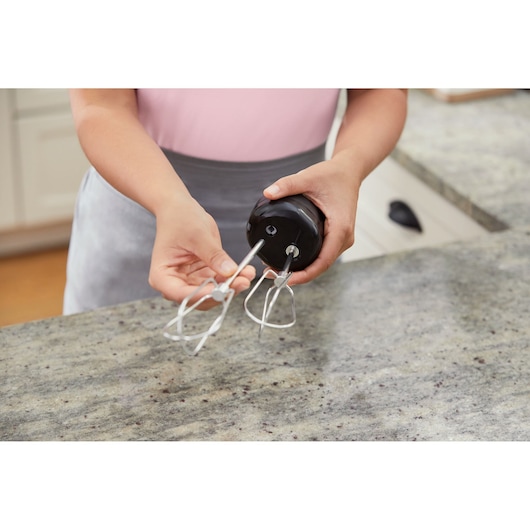 BLACK+DECKER BCKM101HM hand mixer being assembled on kitchen counter, close-up of hands and metal beaters.