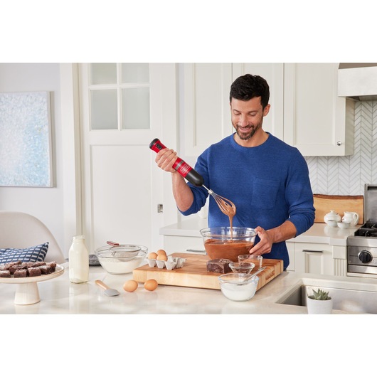 BLACKDECKER BCKM101WHFF hand mixer used to stir cake batter in kitchen with baking ingredients on counter.