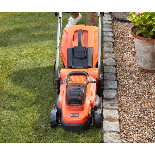 BLACKDECKER BCMW3318N cordless lawn mower top view on grass near stone border.