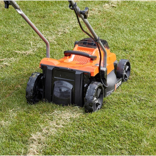 BLACKDECKER BCMW3318N lawn mower close-up on grass, orange and black body, rear view.