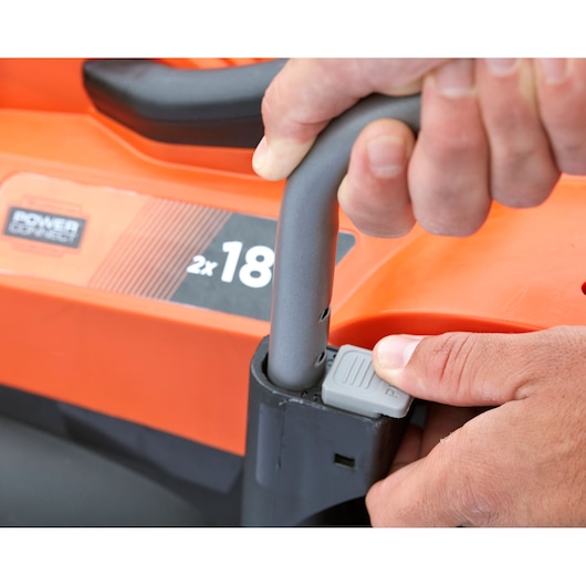 Close-up of BLACKDECKER BCMW3318N lawn mower handle adjustment with hands, orange and black body visible.