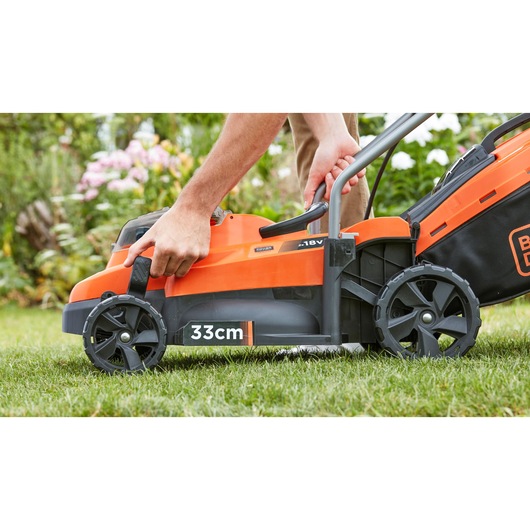 Photo of BLACK+DECKER BCMW3318N lawn mower, orange and black, side view, user adjusting handle, 33cm cutting width.
