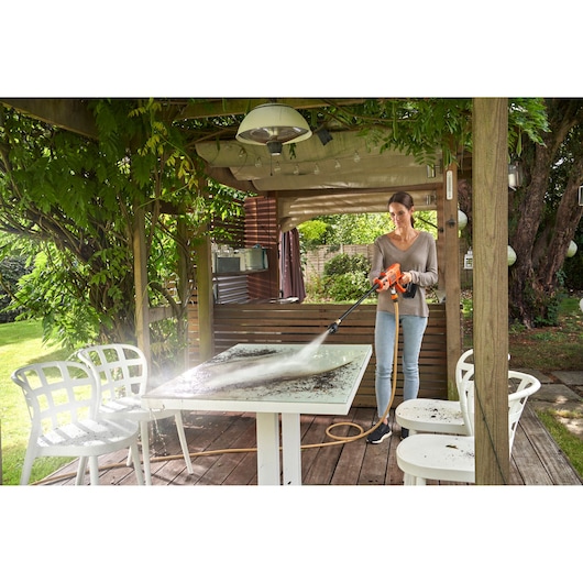 BLACKDECKER BCPC18B pressure washer cleaning outdoor table on patio with person using product.