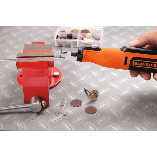 Photo of BLACK+DECKER BCRT8I rotary tool in use, with accessories and a red vise on a metal-patterned surface.