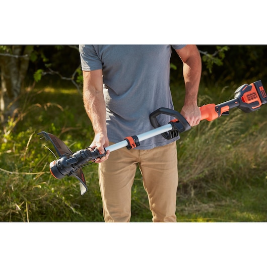 Photo of BLACK+DECKER BCSTE636L1 grass trimmer in use outdoors, focusing on handle and cutting head.