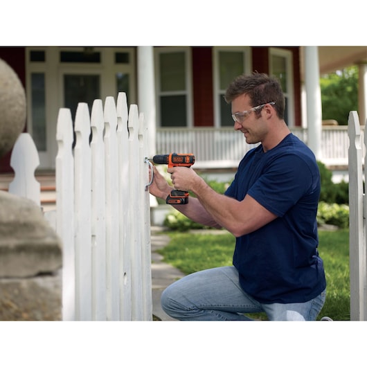 BLACKDECKER BDCDD12K cordless drill used on a white fence outdoors, product in hand.