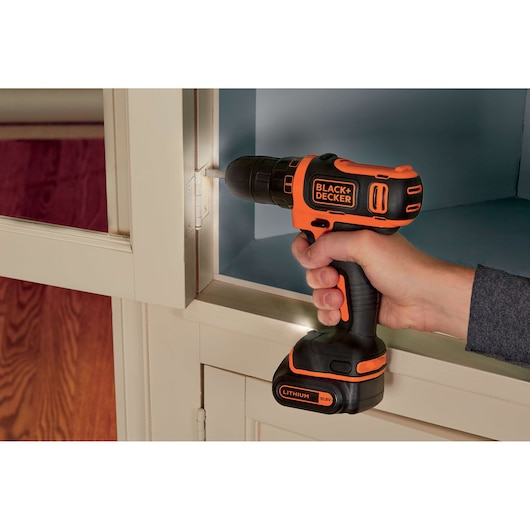 BLACK+DECKER BDCDD12K cordless drill with lithium battery being used to fasten screw in cabinet.