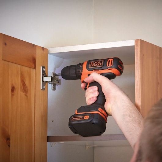 Photo of BLACK+DECKER BDCDD12K cordless drill being used on a cabinet hinge, close-up view.