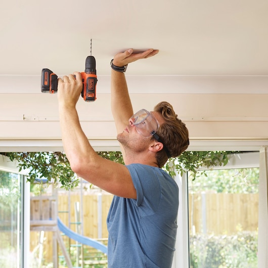 BLACKDECKER BDCDD12K cordless drill with orange and black design in use drilling into ceiling indoors.