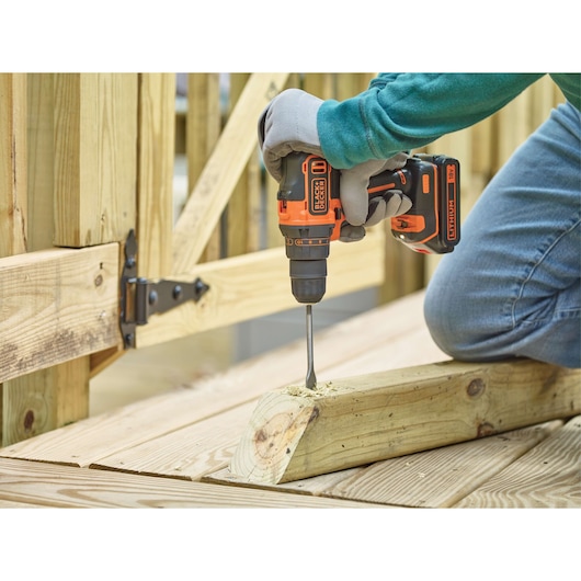 BLACKDECKER BDCDD186K cordless drill used to bore into wood outdoors, operator wearing gloves.