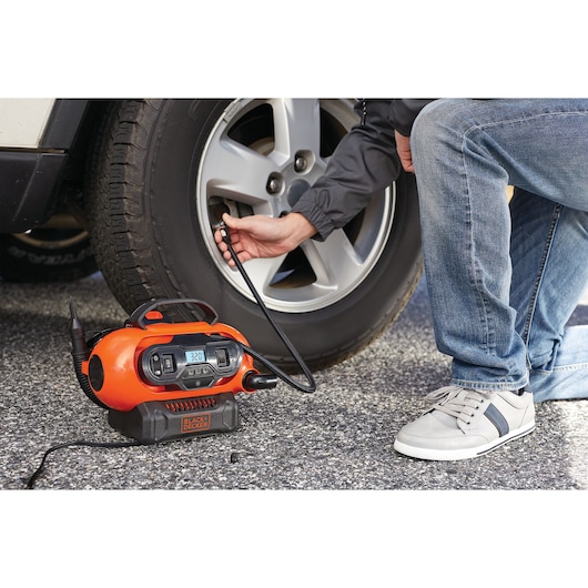 BLACKDECKER BDCINF18N orange portable inflator in use inflating car tire outdoors.