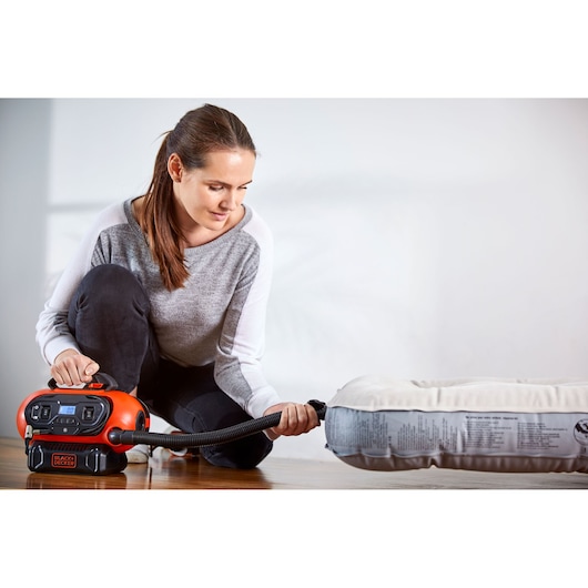 BLACKDECKER BDCINF18N air inflator used to inflate a mattress indoors, product in use with hose attached.