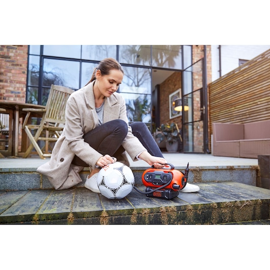 BLACKDECKER BDCINF18N orange portable inflator in use to inflate a white soccer ball outdoors.