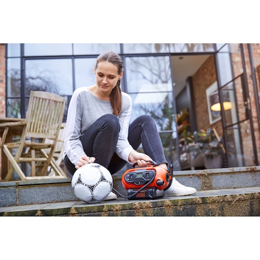 BLACKDECKER BDCINF18N portable air inflator beside a soccer ball outdoors, product in use by a seated person.