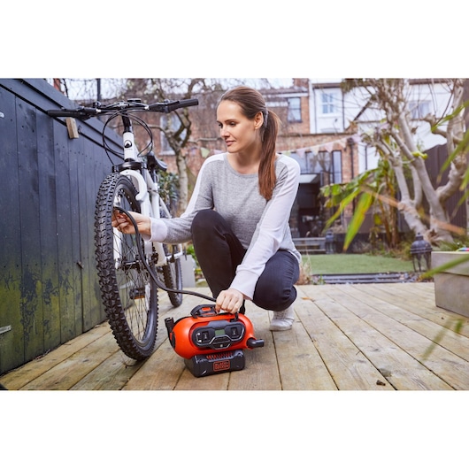 BLACKDECKER BDCINF18N portable inflator being used to pump a bicycle tire on a wooden deck outdoors.