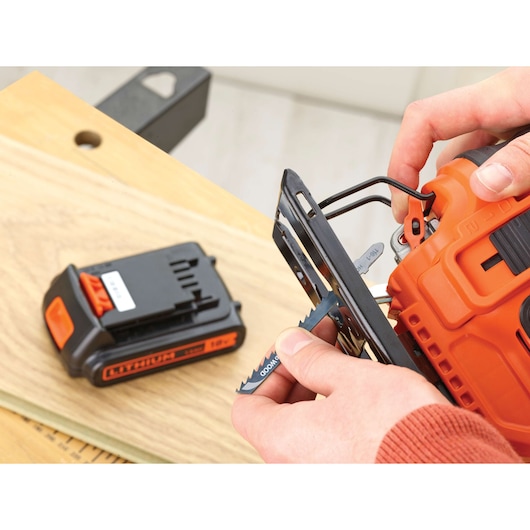 BLACKDECKER BDCJS18 cordless jigsaw with orange and black body, close-up of blade installation, battery on side.