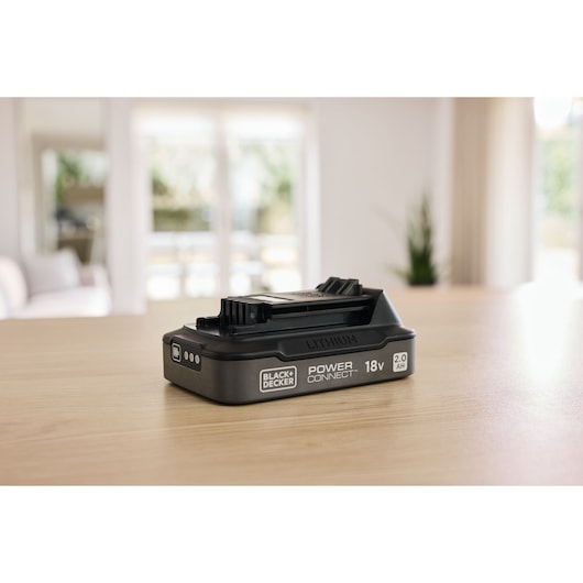 BLACK+DECKER BDL2018S 18V lithium battery for power tools on wooden table, angled side view.