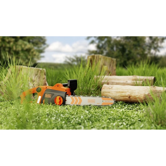 Photo of BLACK+DECKER BECS1835 chainsaw lying on grass with logs in the background, outdoor setting.