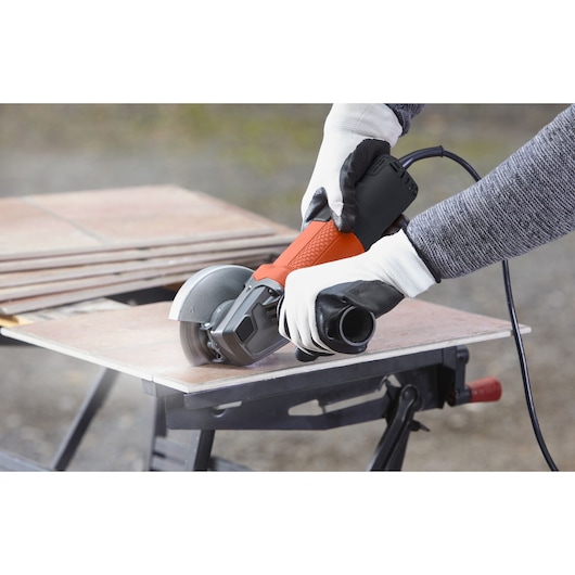 BLACKDECKER BEG110 angle grinder held with gloves, cutting tile on a workbench, product in use.