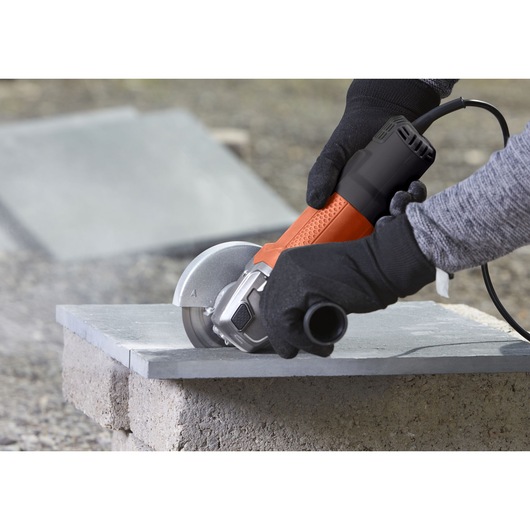 BLACKDECKER BEG110 angle grinder in use cutting a stone slab, close up of hands wearing gloves.