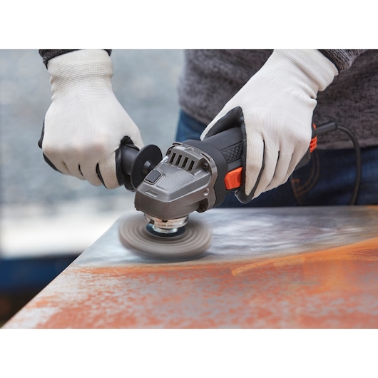 BLACKDECKER BEG220 angle grinder in use for surface grinding, shown close up with gloved hands.