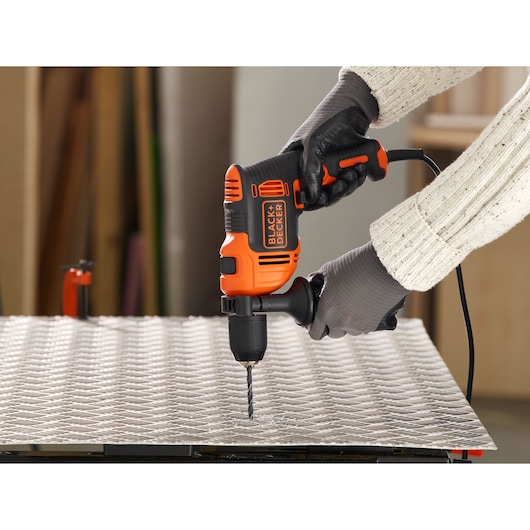 BLACK+DECKER BEH710SA32 corded drill in use on a metal sheet, user wearing gloves and sweater.