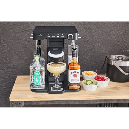 Photo of BLACK+DECKER BEHB101 cocktail maker with bottles and a margarita glass, garnishes, and ice bucket on a wooden table.