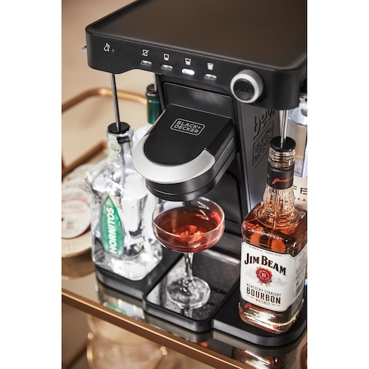 BLACK+DECKER BEHB101 cocktail machine on bar cart with liquor bottles and a cocktail glass, front angle.