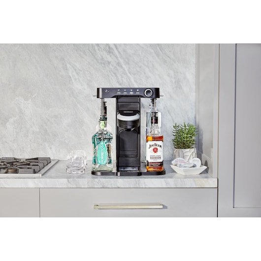 BLACKDECKER BEHB101 drink maker with two liquor bottles on a kitchen counter, marble backsplash, glassware, and plant.