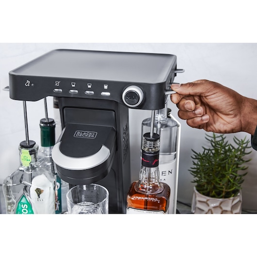 BLACK+DECKER BEHB101 drink mixer on counter with liquor bottles and hand operating lever, front angle.