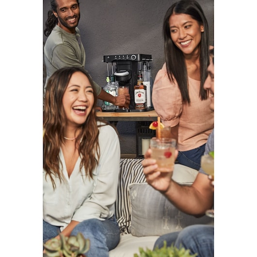 Photo of BLACK+DECKER BEHB101 coffee maker on a table with bottles and glasses, people gathered around in casual setting.