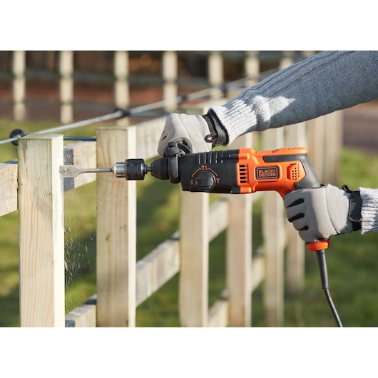 BLACKDECKER BEHS01K corded hammer drill in use drilling into wooden fence outdoors.