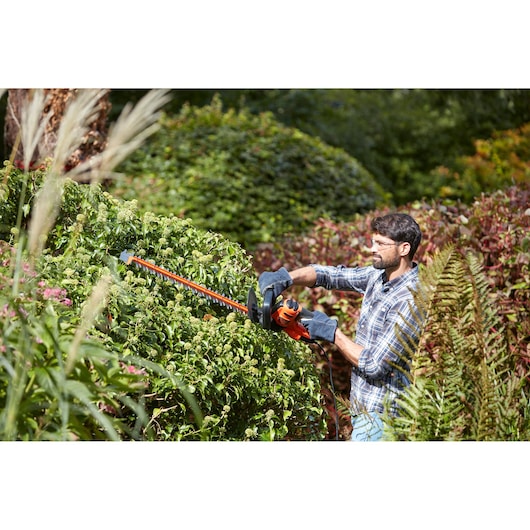 BLACKDECKER BEHTS401 hedge trimmer in use outdoors trimming green bushes.